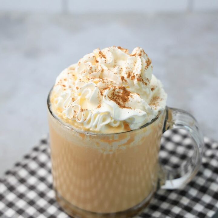 Pumpkin Hot Chocolate in a clear glass on a plaid napkin on a concrete backdrop