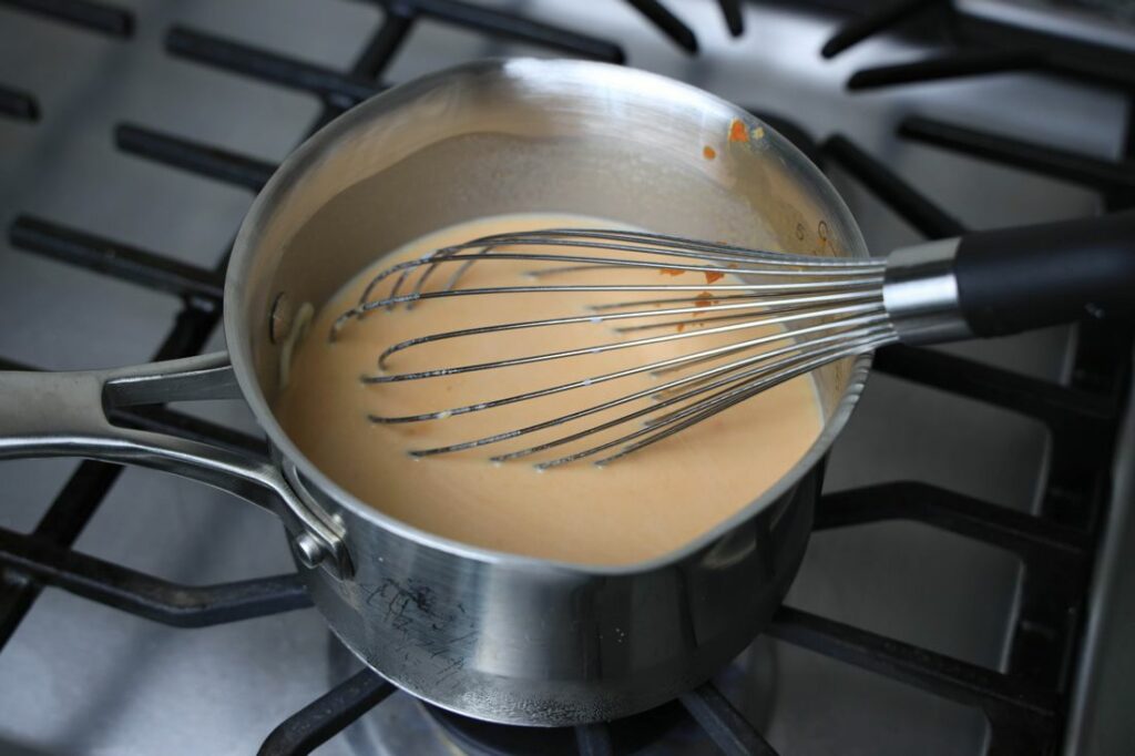 Pumpkin hot chocolate in the sauce pan with a whisk on top.