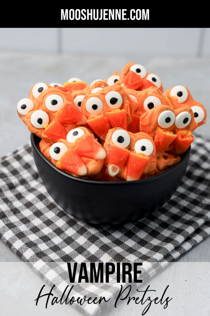 Pretzels with candy eyes and candy corn as fangs. In a black bowl on a plaid napkin.