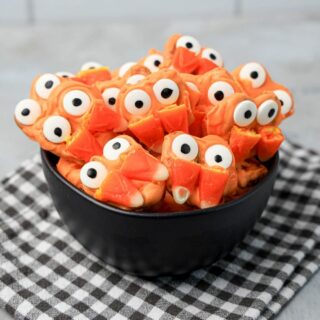 Pretzels with candy eyes and candy corn as fangs. In a black bowl on a plaid napkin.
