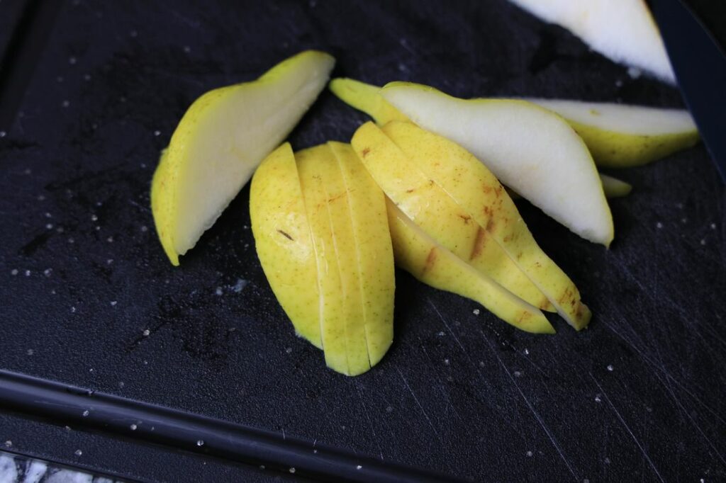 Bartlett pears sliced on a black cutting board.