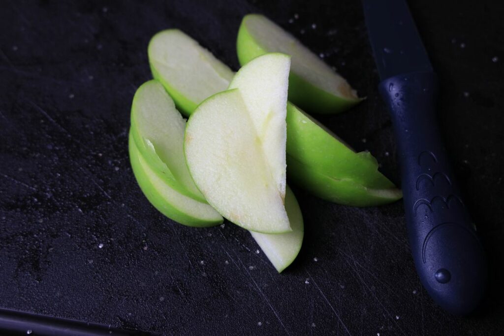 Granny smith apples sliced on a cutting board.