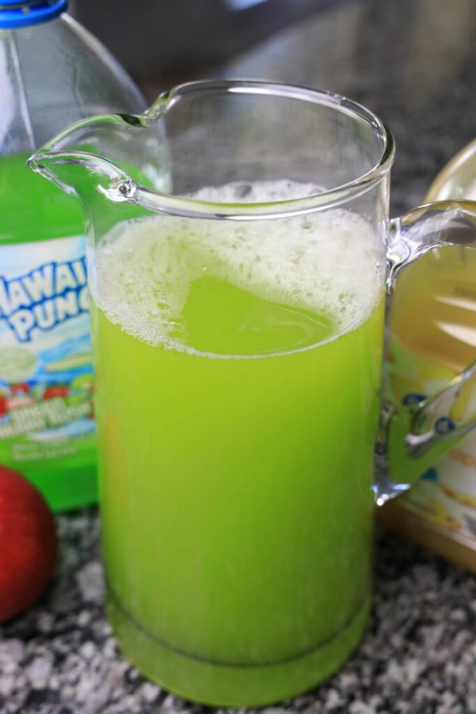 Pineapple juice and green berry punch in a glass pitcher.