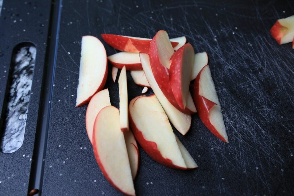Sliced red apples on a black cutting board.