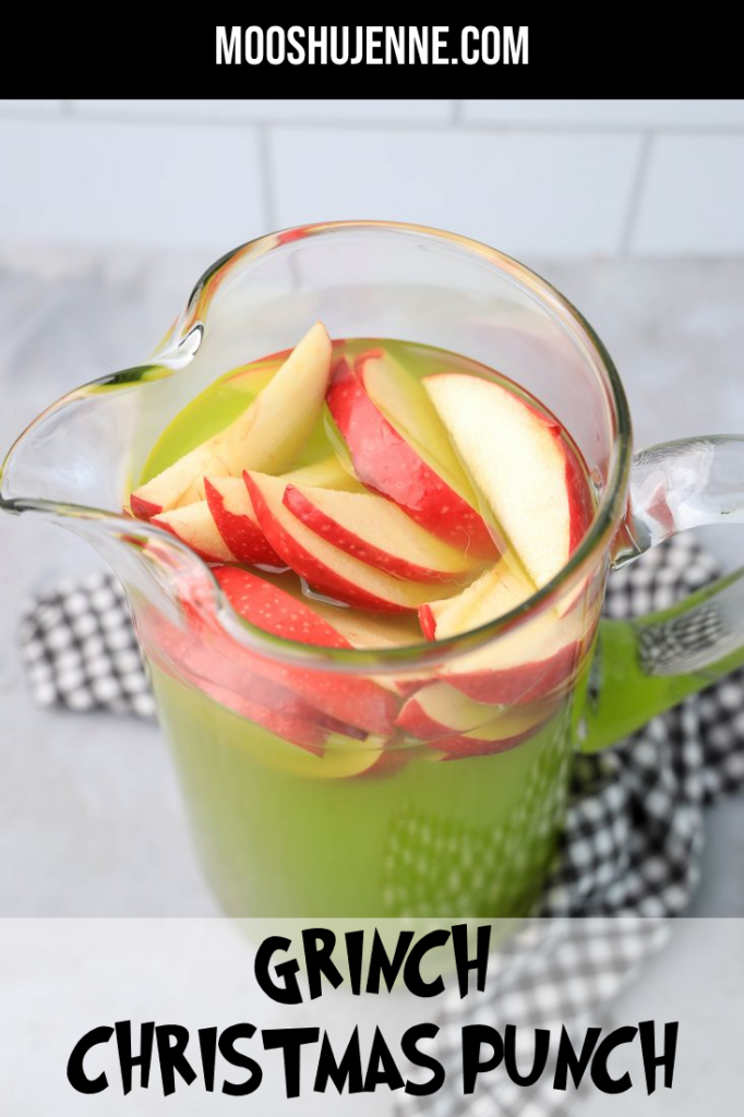 Grinch Christmas Punch with red apples in a glass pitcher on a gray plaid napkin.