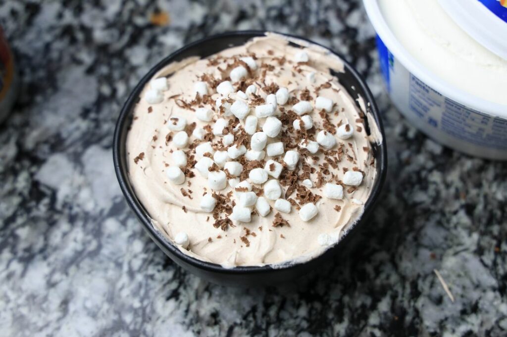 Whipped hot chocolate dip in a black bowl with marshmallow bits and chocolate over the top.