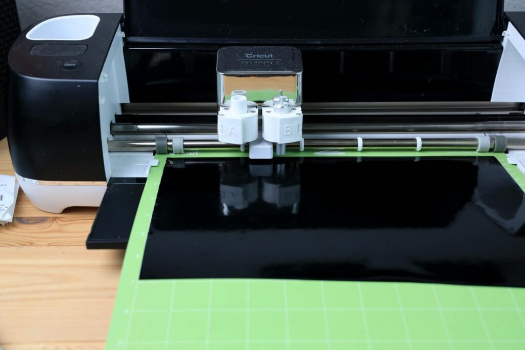 Green cutting mat in the cricut machine with black vinyl.