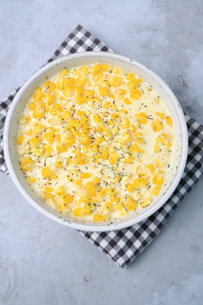 Parmesan Creamed Corn in a stone dish with a plaid napkin on a faux concrete backdrop.