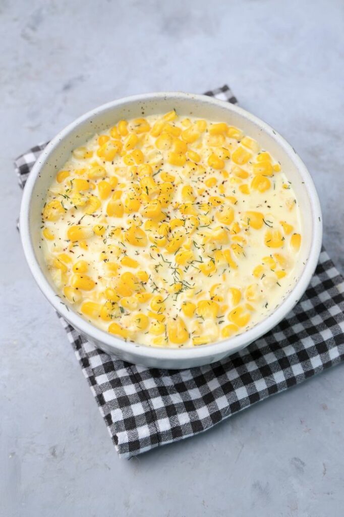 Parmesan Creamed Corn in a stone dish with a plaid napkin on a faux concrete backdrop.