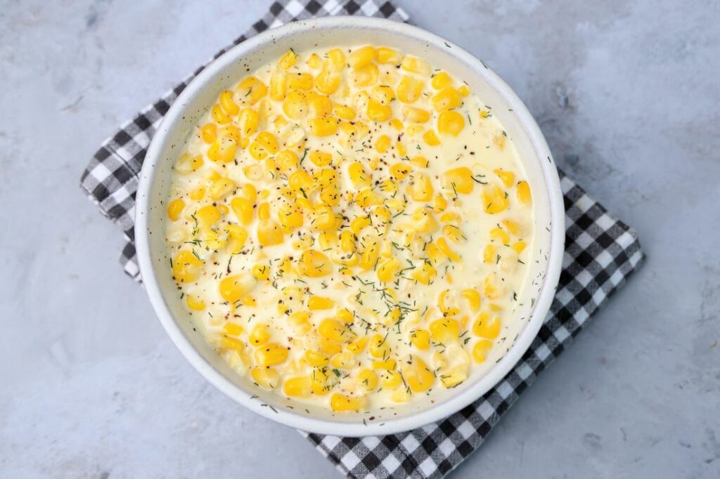 Parmesan Creamed Corn in a stone dish with a plaid napkin on a faux concrete backdrop.