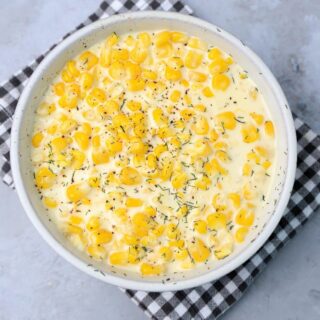 Parmesan Creamed Corn in a stone dish with a plaid napkin on a faux concrete backdrop.