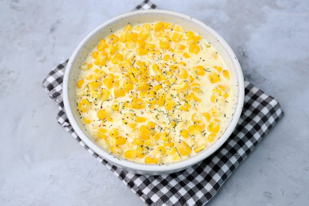 Parmesan Creamed Corn in a stone dish with a plaid napkin on a faux concrete backdrop.