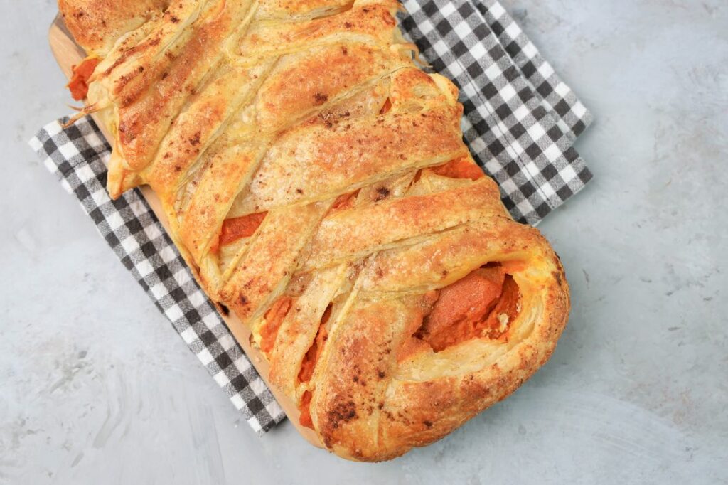 Pumpkin puff pastry braid on a plaid napkin with a faux concrete back drop.