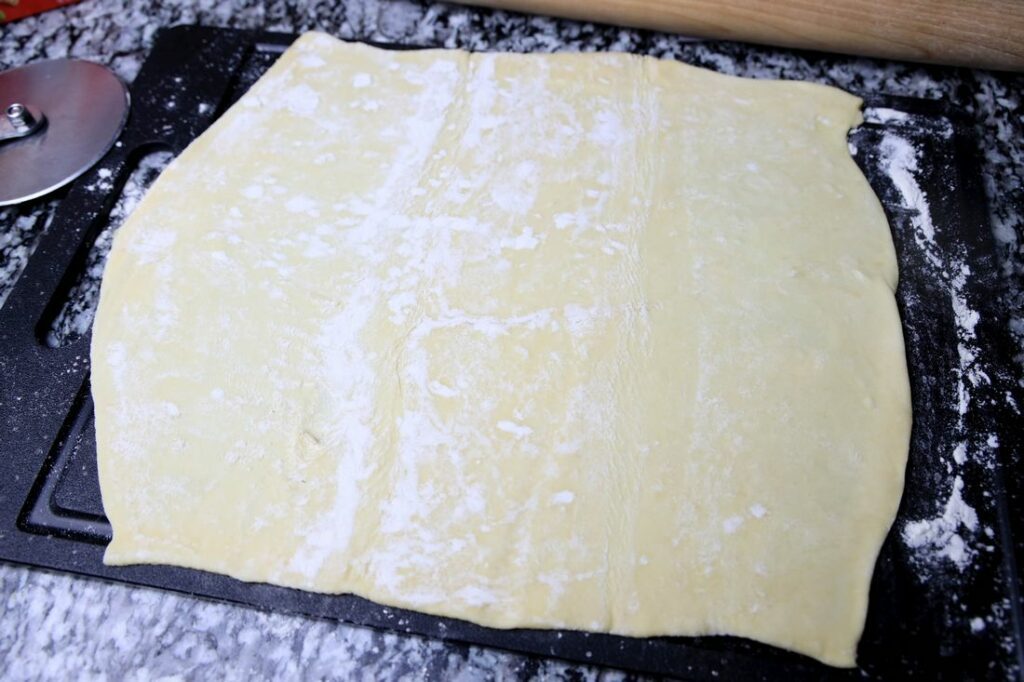 Puff pastry dough on a black cutting board rolled out.