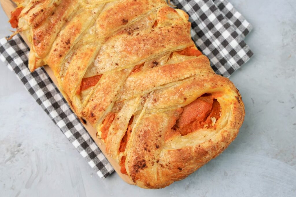 Pumpkin puff pastry braid on a plaid napkin with a faux concrete back drop.