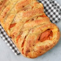 Pumpkin puff pastry braid on a plaid napkin with a faux concrete back drop.