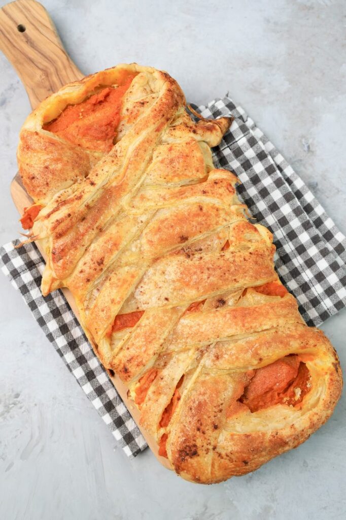 Pumpkin puff pastry braid on a plaid napkin with a faux concrete back drop.