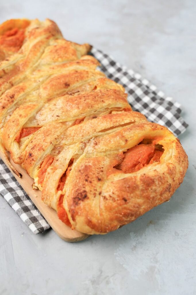 Pumpkin puff pastry braid on a plaid napkin with a faux concrete back drop.