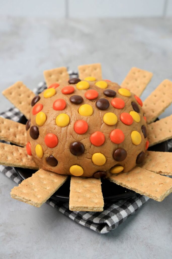 Reese's pieces peanut butter dip with reese's pieces on top and graham crackers along the sides for serving.