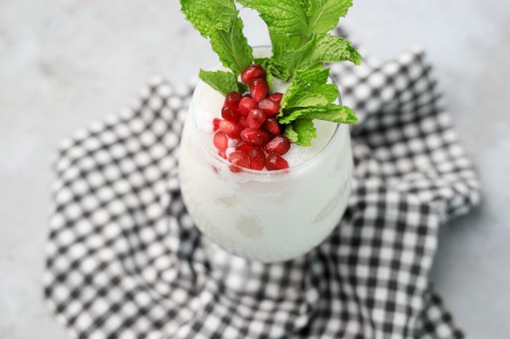 White Christmas Mojito in a glass with pomegranate and mint leaves on a gray plaid napkin.