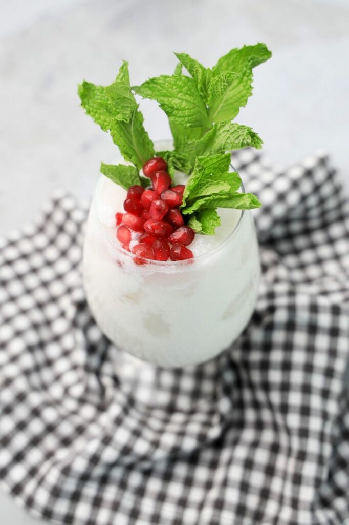 White Christmas Mojito in a glass with pomegranate and mint leaves on a gray plaid napkin.