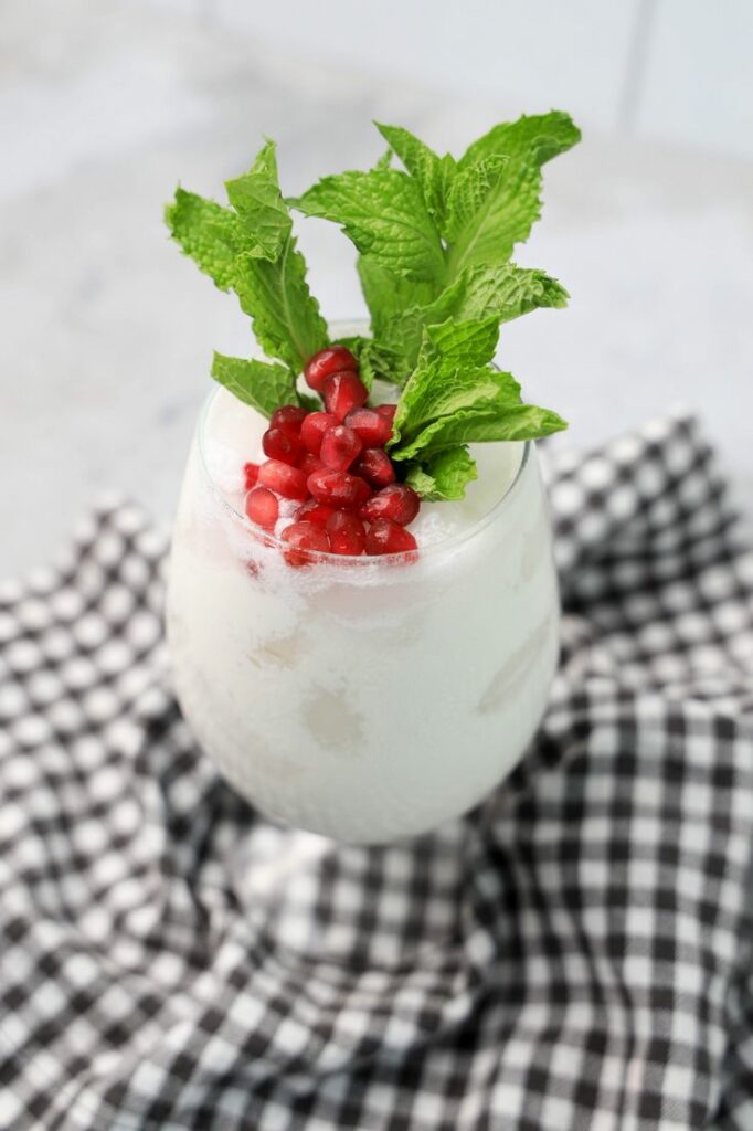 White Christmas Mojito in a glass with pomegranate and mint leaves on a gray plaid napkin.