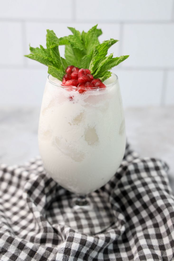 White Christmas Mojito in a glass with pomegranate and mint leaves on a gray plaid napkin.