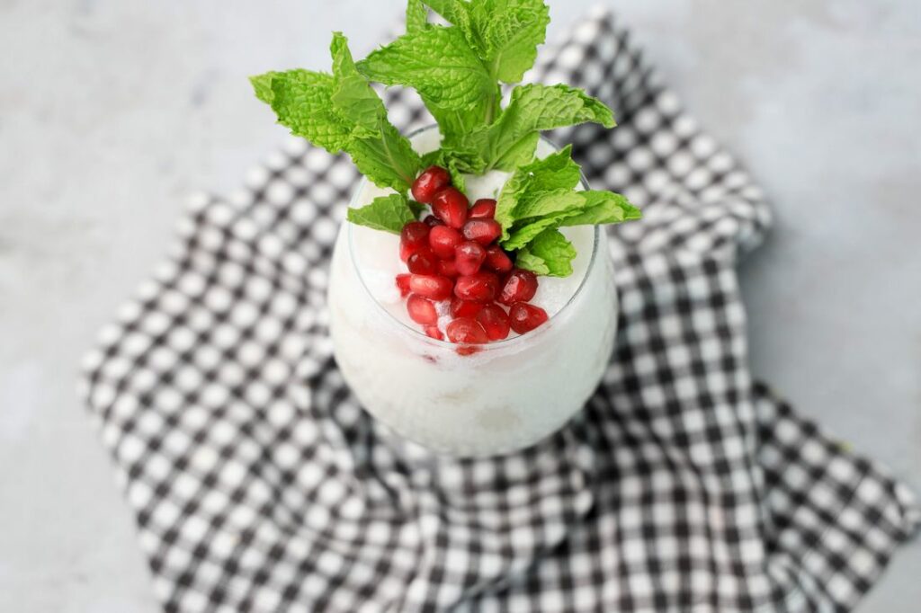 White Christmas Mojito in a glass with pomegranate and mint leaves on a gray plaid napkin.