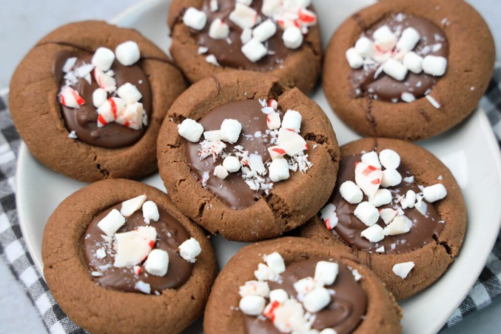Hot Chocolate Peppermint Thumbprint Cookies on a white plate with gray plaid napkin on a faux concrete backdrop.