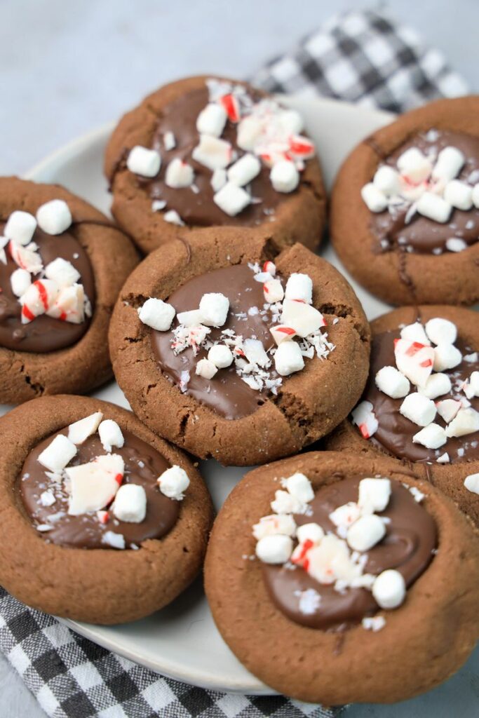 Hot Chocolate Peppermint Thumbprint Cookies on a white plate with gray plaid napkin on a faux concrete backdrop.