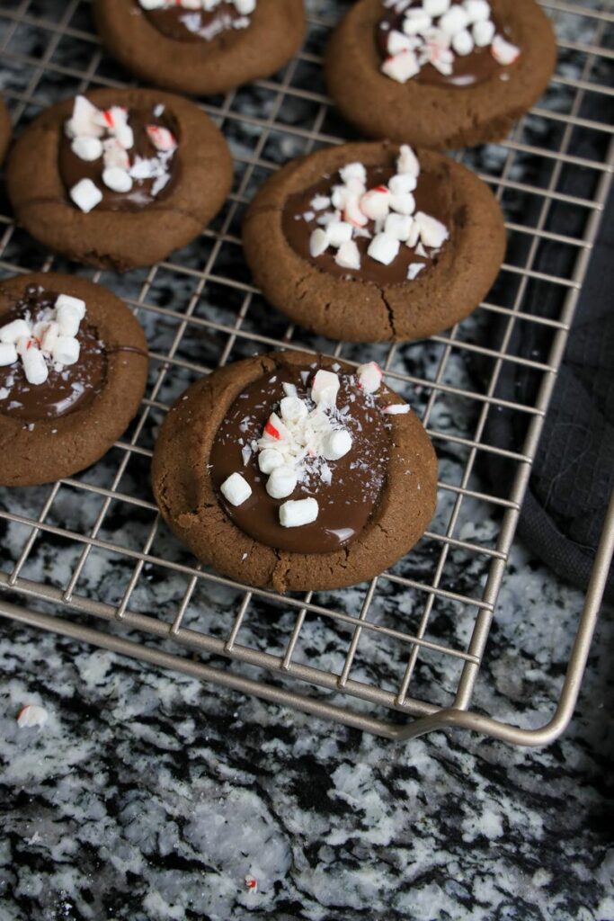 Hot chocolate peppermint thumbprint cookies topped with mini marshmallow bits and crushed peppermint.