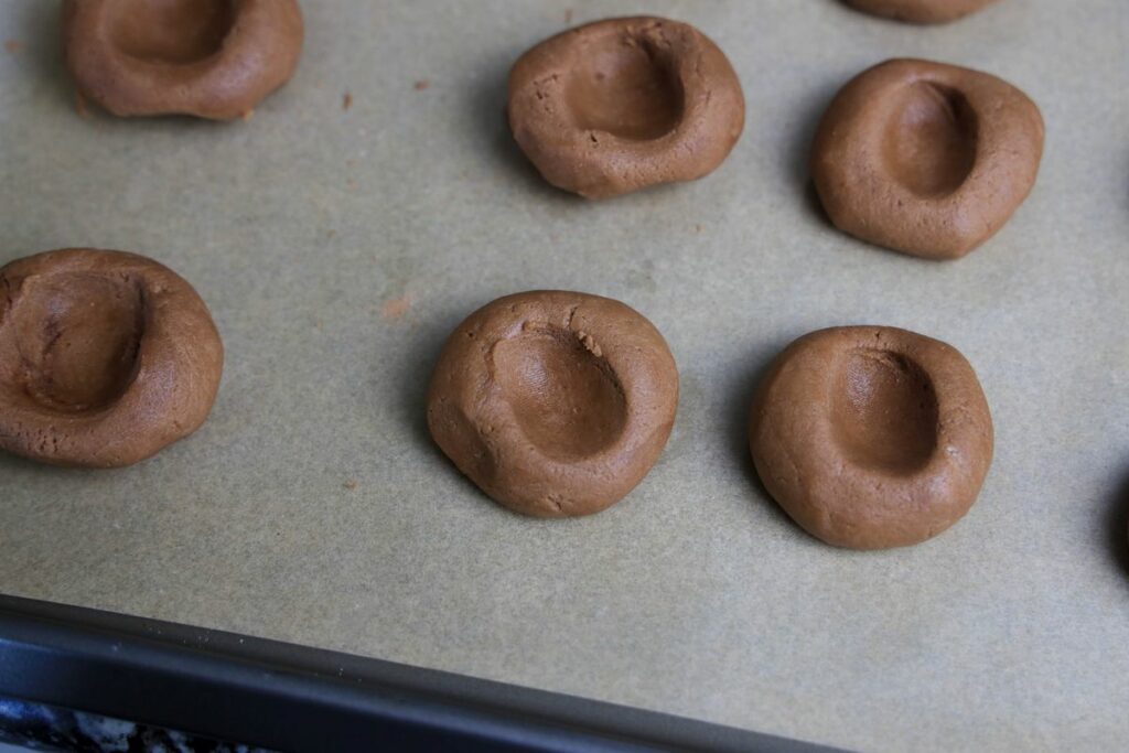 Cookie dough with thumbprints on a parchment lined baking sheet.