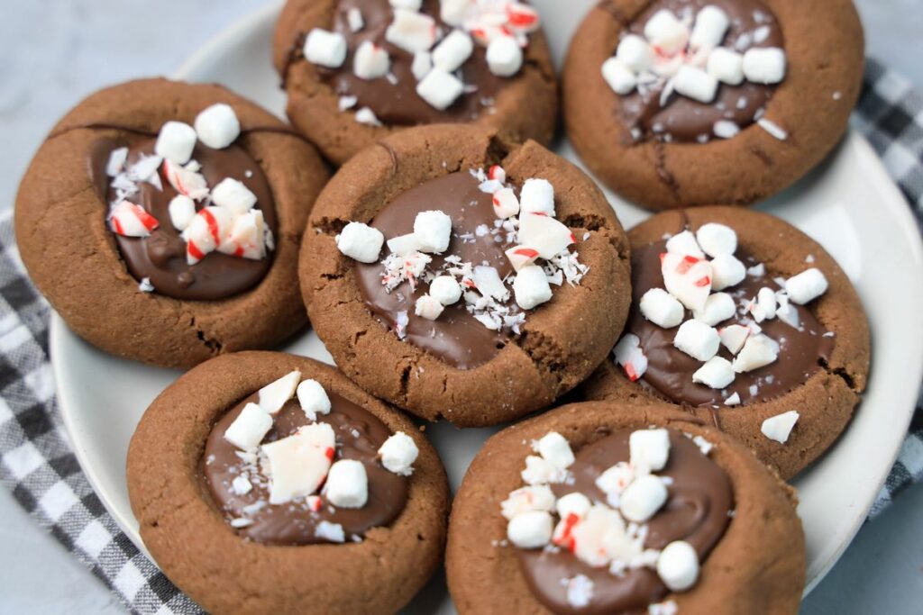 Hot Chocolate Peppermint Thumbprint Cookies on a white plate with gray plaid napkin on a faux concrete backdrop.