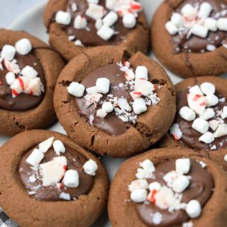 Hot Chocolate Peppermint Thumbprint Cookies on a white plate with gray plaid napkin on a faux concrete backdrop.