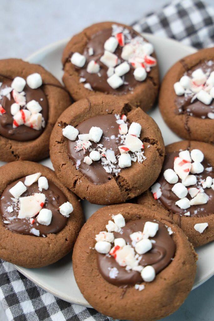 Hot Chocolate Peppermint Thumbprint Cookies on a white plate with gray plaid napkin on a faux concrete backdrop.