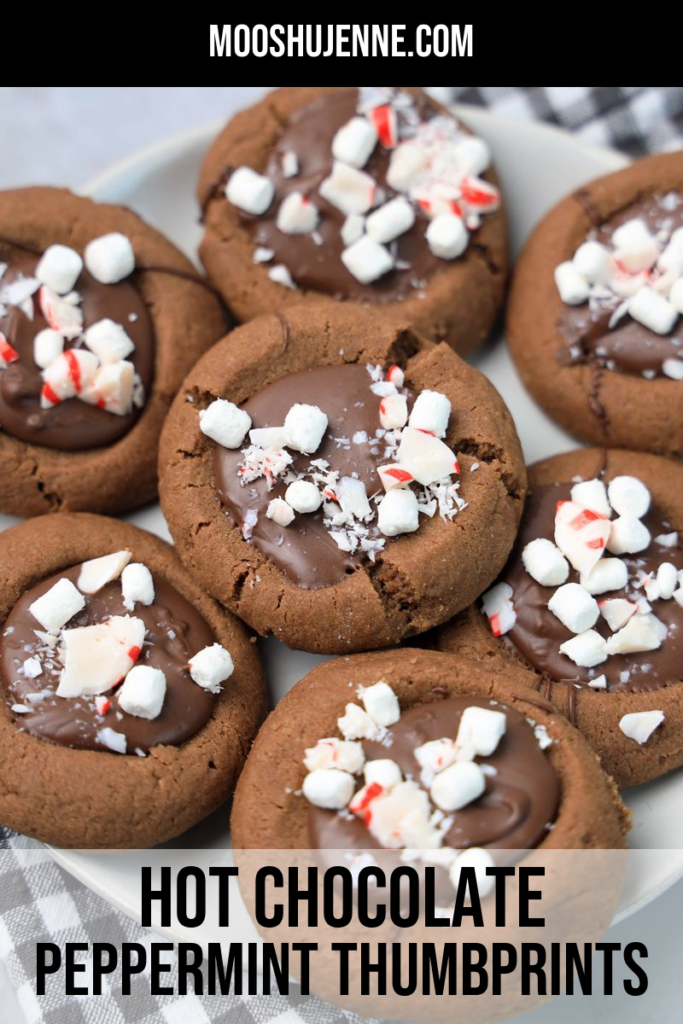 Hot Chocolate Peppermint Thumbprint Cookies on a white plate with gray plaid napkin on a faux concrete backdrop.