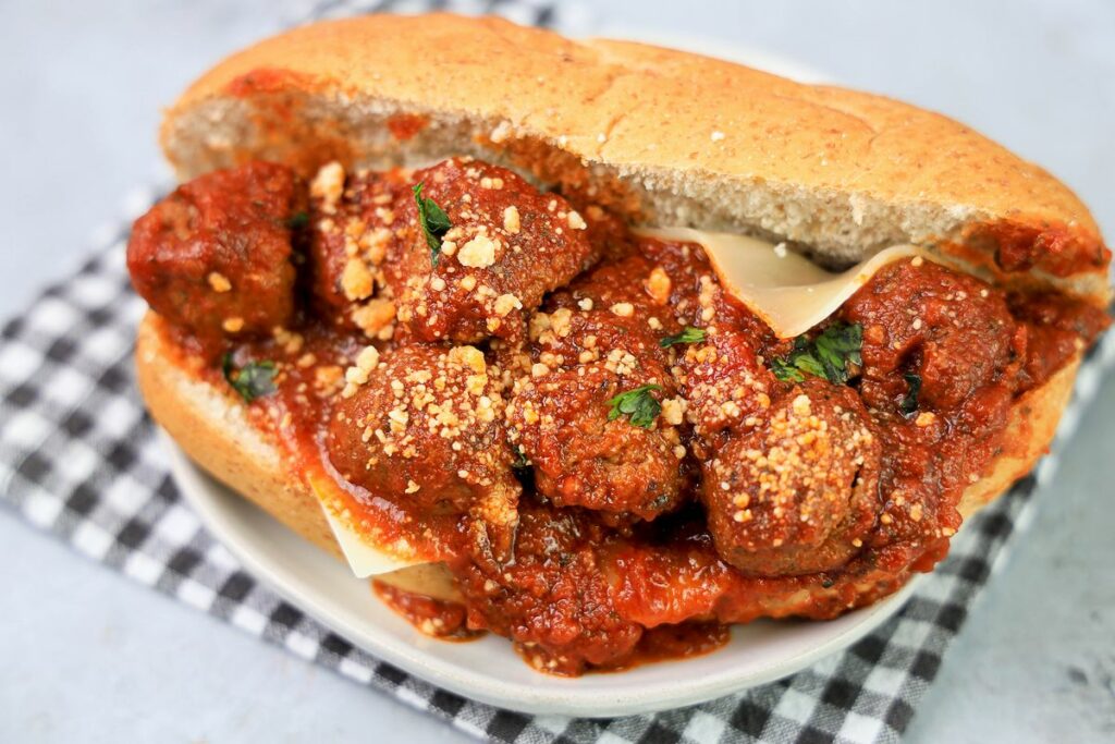 Slow Cooker Italian Meatball Subs on a white plate with a gray plaid napkin on a faux concrete backdrop.