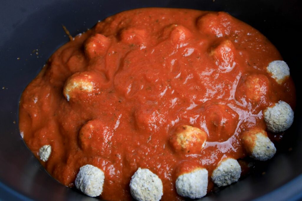 Frozen meatballs in a crockpot topped with red sauce.