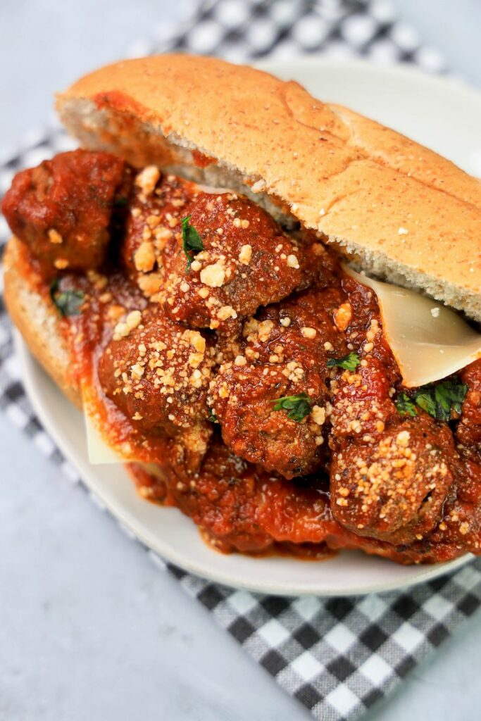 Slow Cooker Italian Meatball Subs on a white plate with a gray plaid napkin on a faux concrete backdrop.