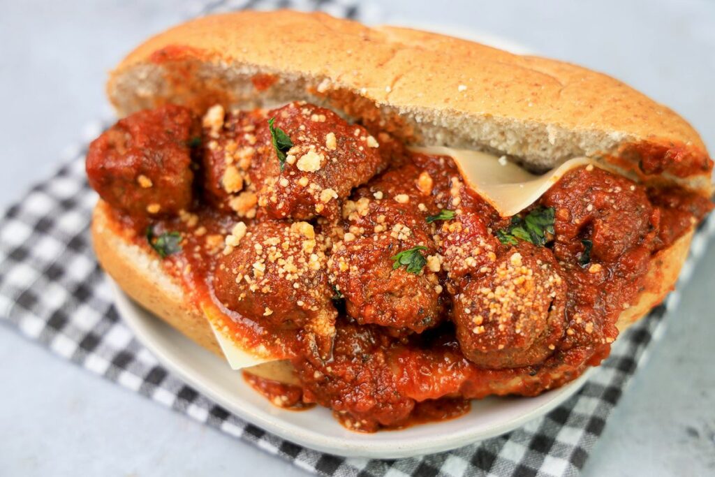 Slow Cooker Italian Meatball Subs on a white plate with a gray plaid napkin on a faux concrete backdrop.