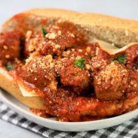 Slow Cooker Italian Meatball Subs on a white plate with a gray plaid napkin on a faux concrete backdrop.