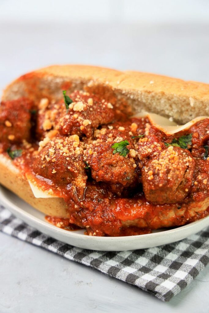 Slow Cooker Italian Meatball Subs on a white plate with a gray plaid napkin on a faux concrete backdrop.