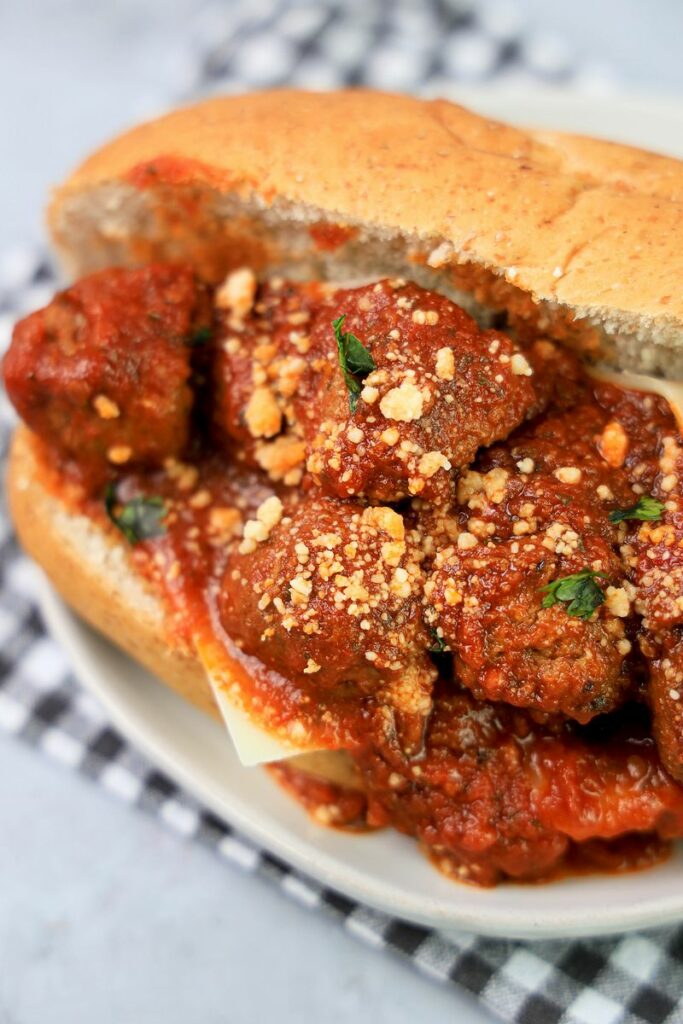 Slow Cooker Italian Meatball Subs on a white plate with a gray plaid napkin on a faux concrete backdrop.