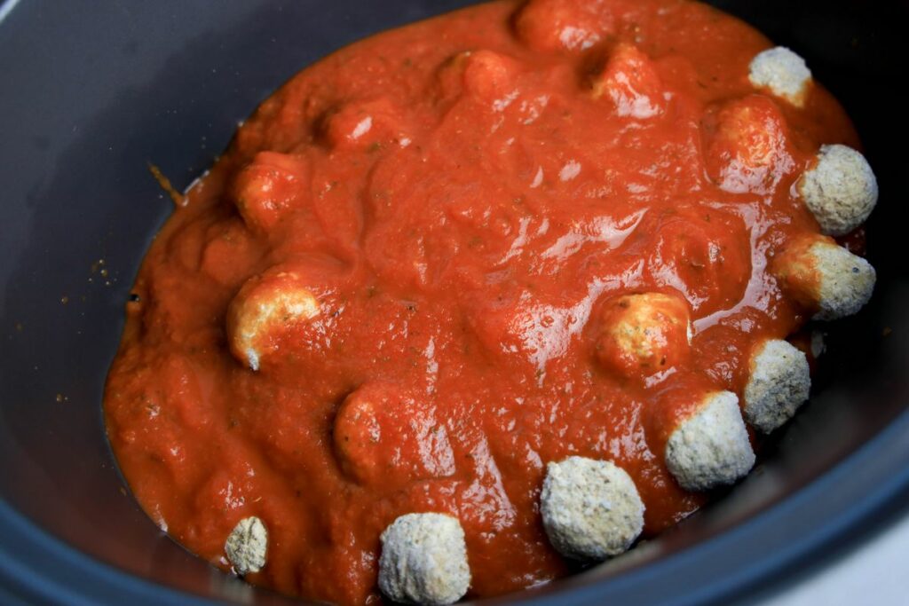 Frozen meatballs in a crockpot topped with red sauce.