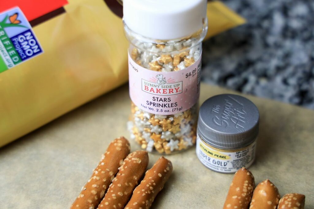 Pretzel rods, sprinkles, and edible gold glitter on parchment paper.