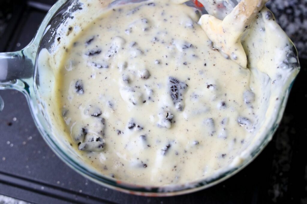 Oreo cookies mixed into the white chocolate in a pyrex bowl.