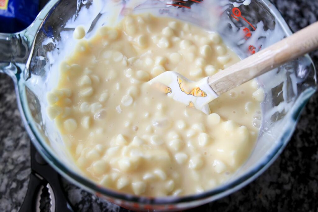 Sweetened condensed milk with white chocolate chips in a pyrex bowl.