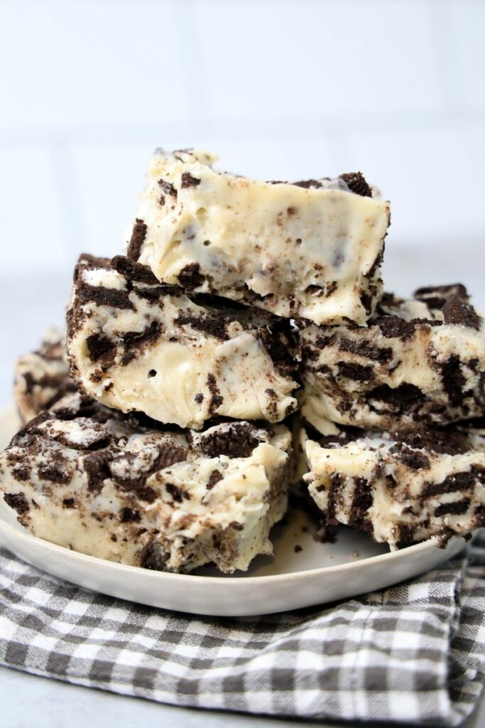 Oreo White Chocolate Fudge stacked on a white plate with gray plaid napkin on a faux concrete back drop.