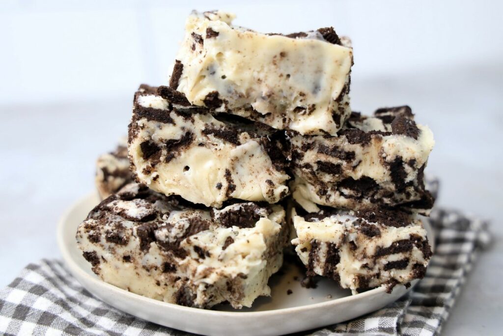 Oreo White Chocolate Fudge stacked on a white plate with gray plaid napkin on a faux concrete back drop.