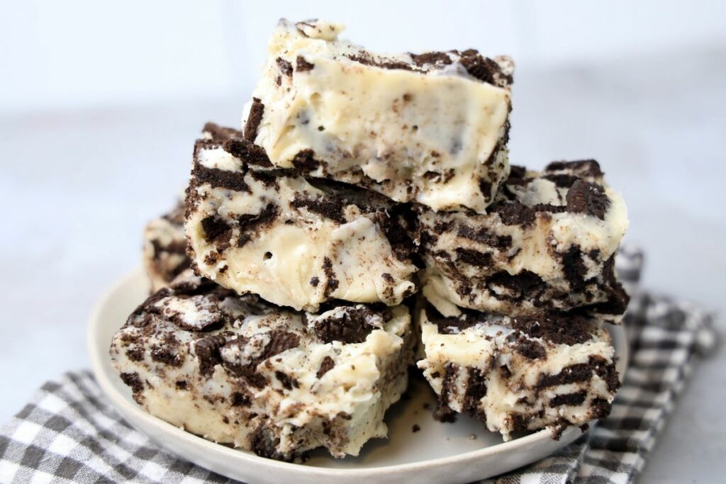 Oreo White Chocolate Fudge stacked on a white plate with gray plaid napkin on a faux concrete back drop.